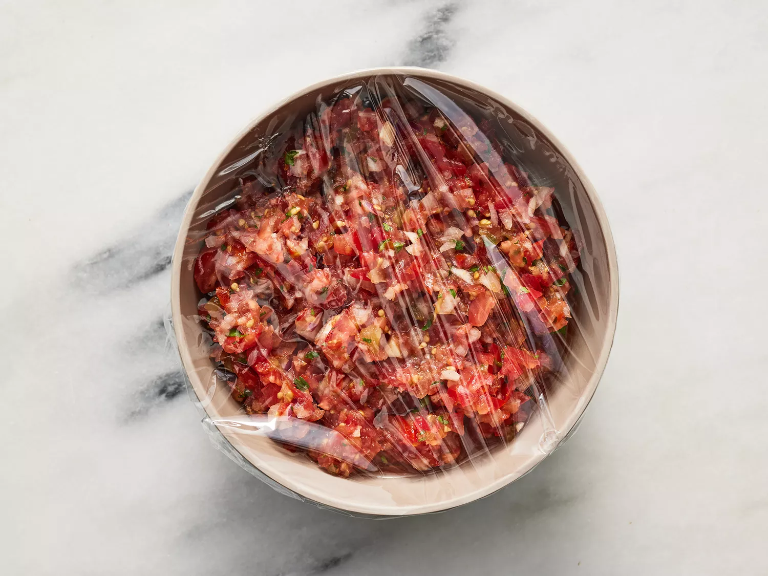 Overhead of salsa in a bowl covered in plastic wrap. 
