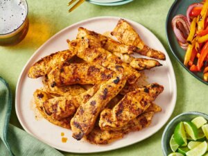 Grilled chicken fajita strips on a plate, surrounded by limes and side dishes for serving