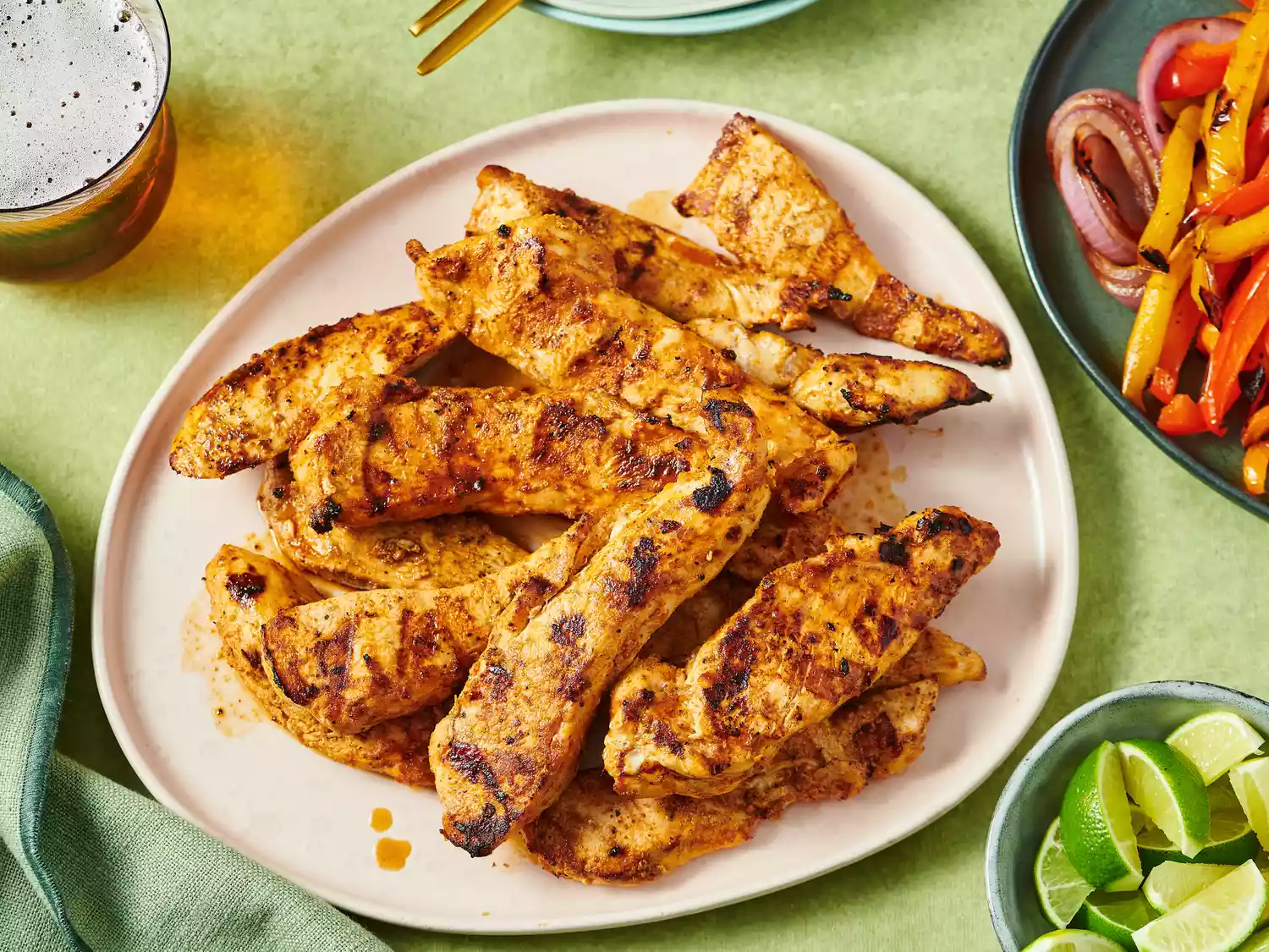 Grilled chicken fajita strips on a plate, surrounded by limes and side dishes for serving