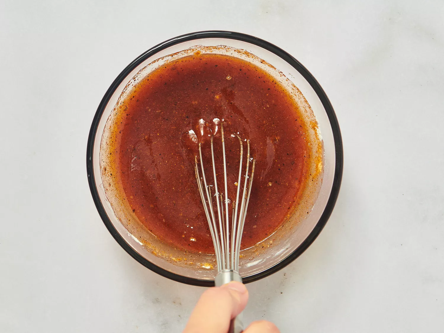 Whisk being used to mix a marinade or sauce in a clear bowl