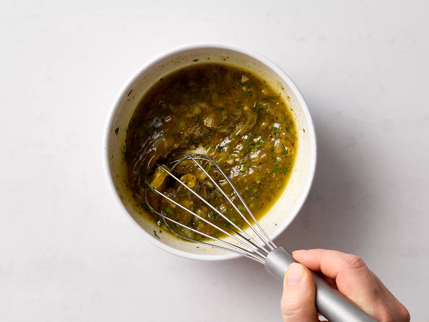 Hand whisking marinade with herbs and spices in a bowl