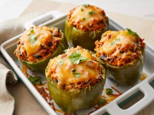 High angle looking at a casserole dish of four vegetarian mexican inspired stuffed peppers garnished with cheese and fresh herbs