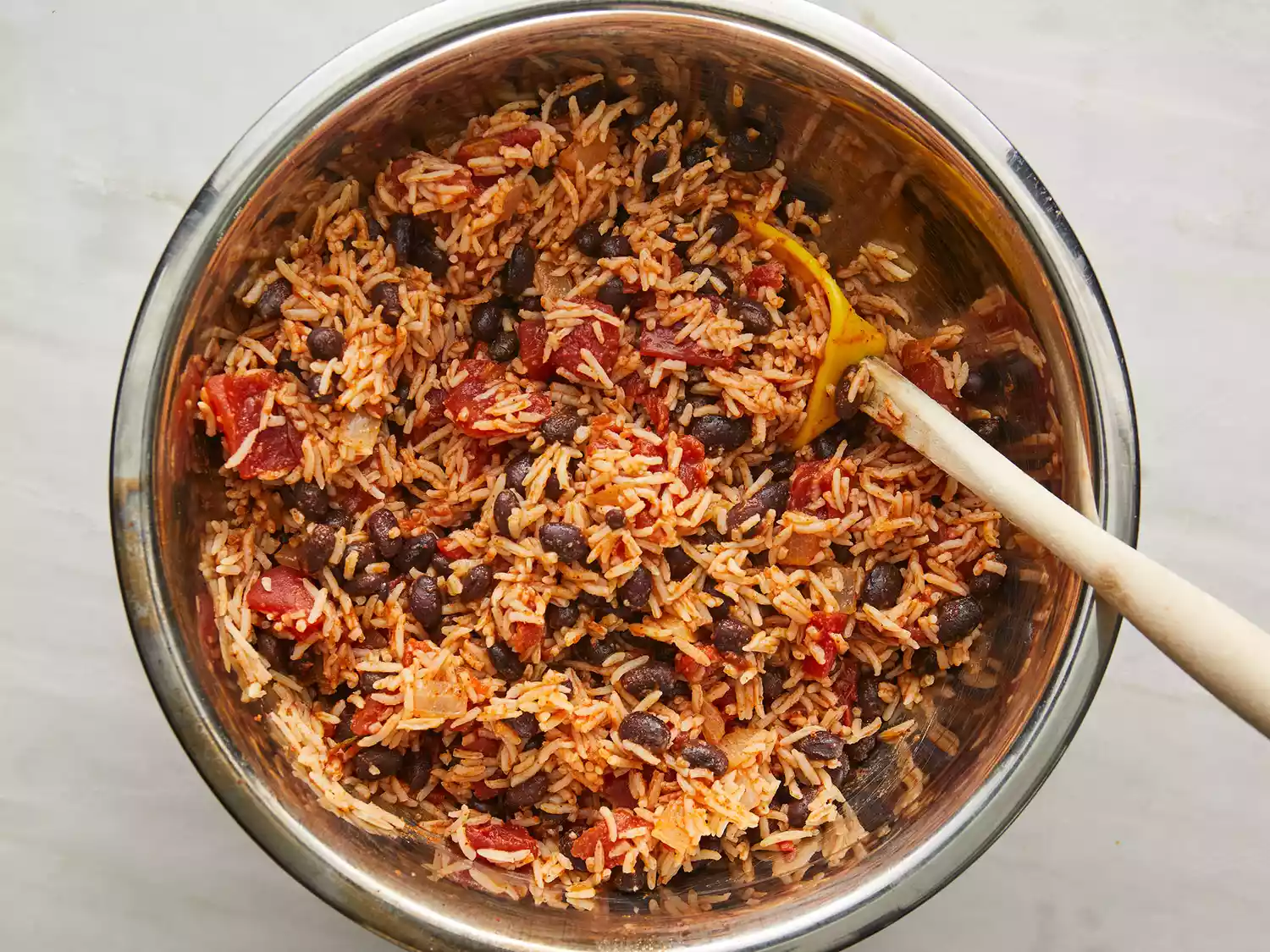 Overhead of rice, black beans, tomatoes, chili powder, garlic salt, and cumin being cooked and stirred together in a pot. 