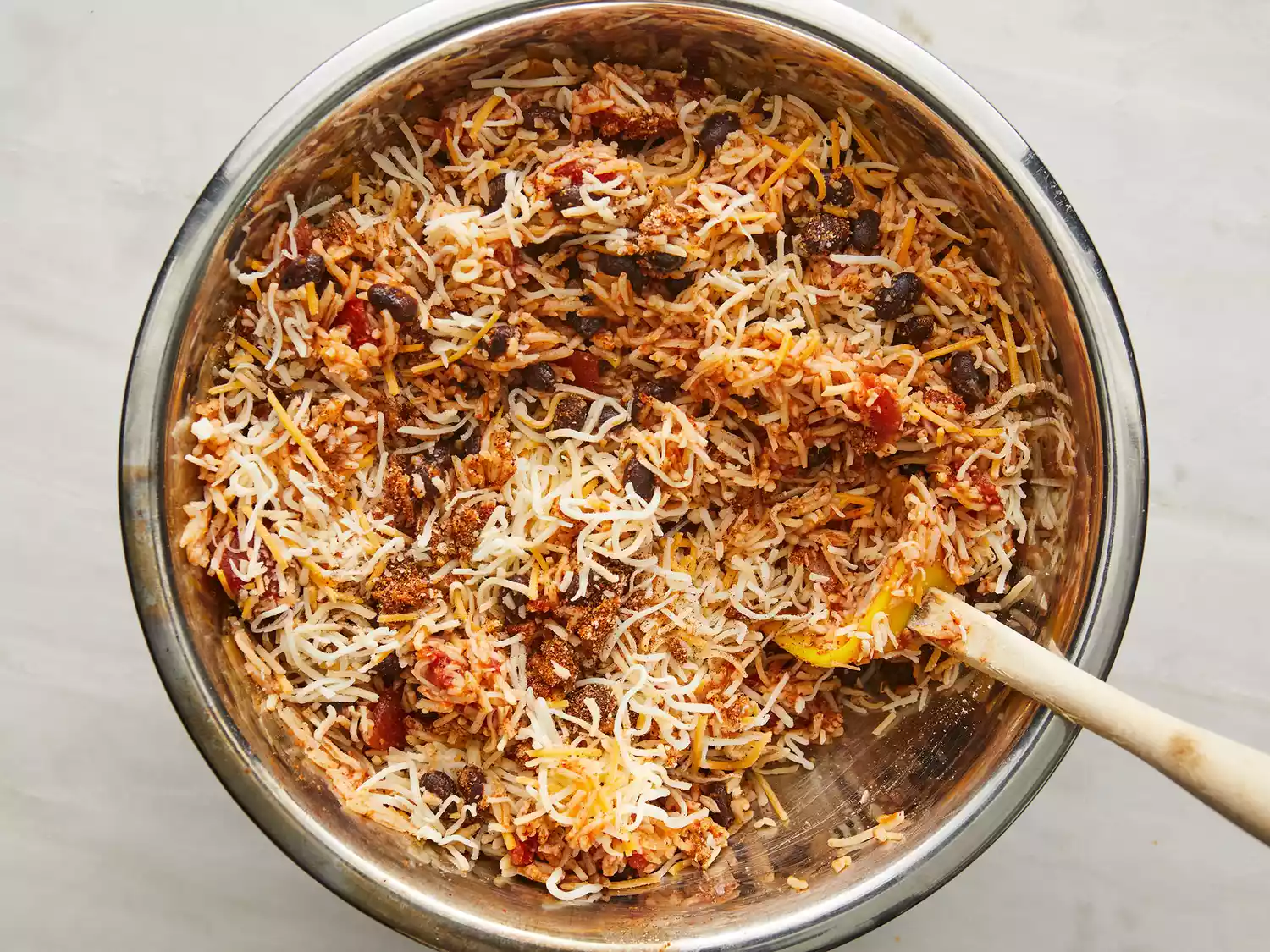 Overhead of shredded cheese being added to a rice and tomato mixture as it cooks in a pot. 