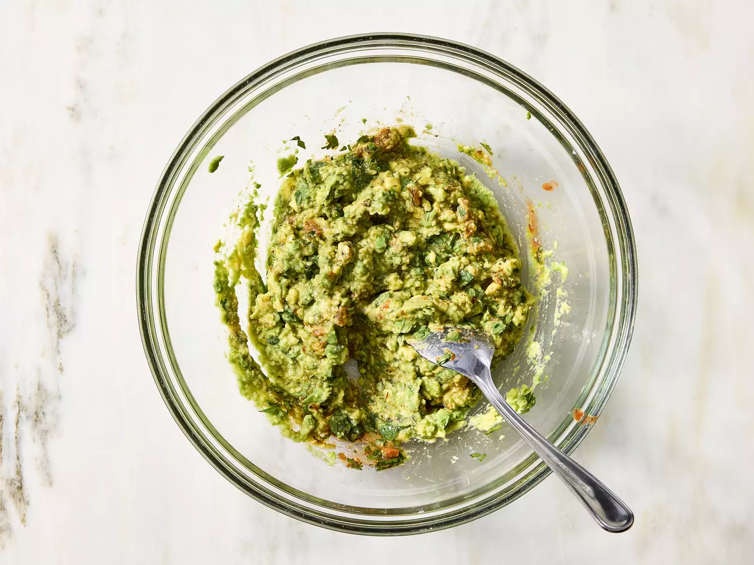 Bowl of mashed guacamole with fork for seven-layer dip.