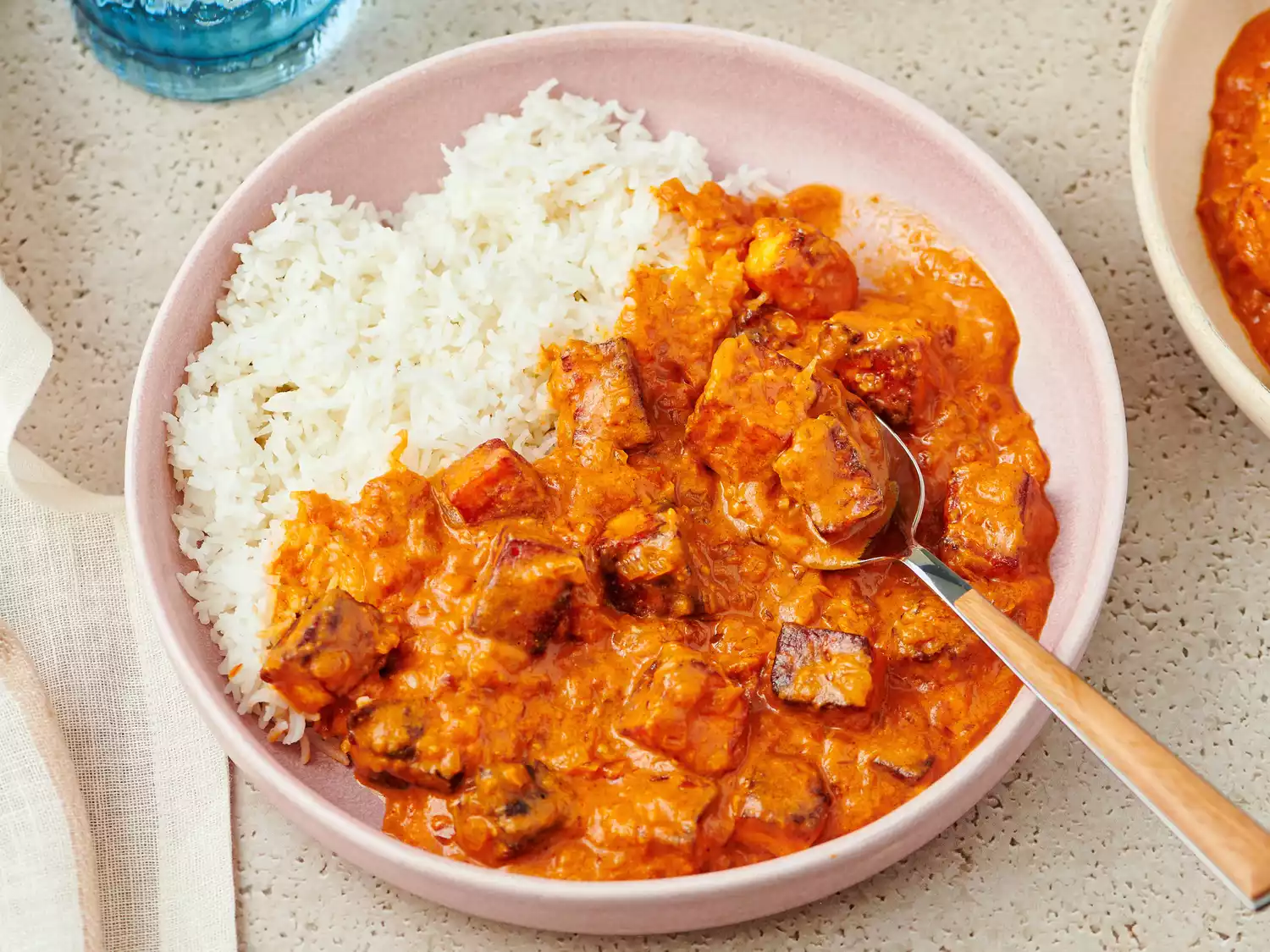 A plate of paneer butter masala served with steamed rice and a spoon