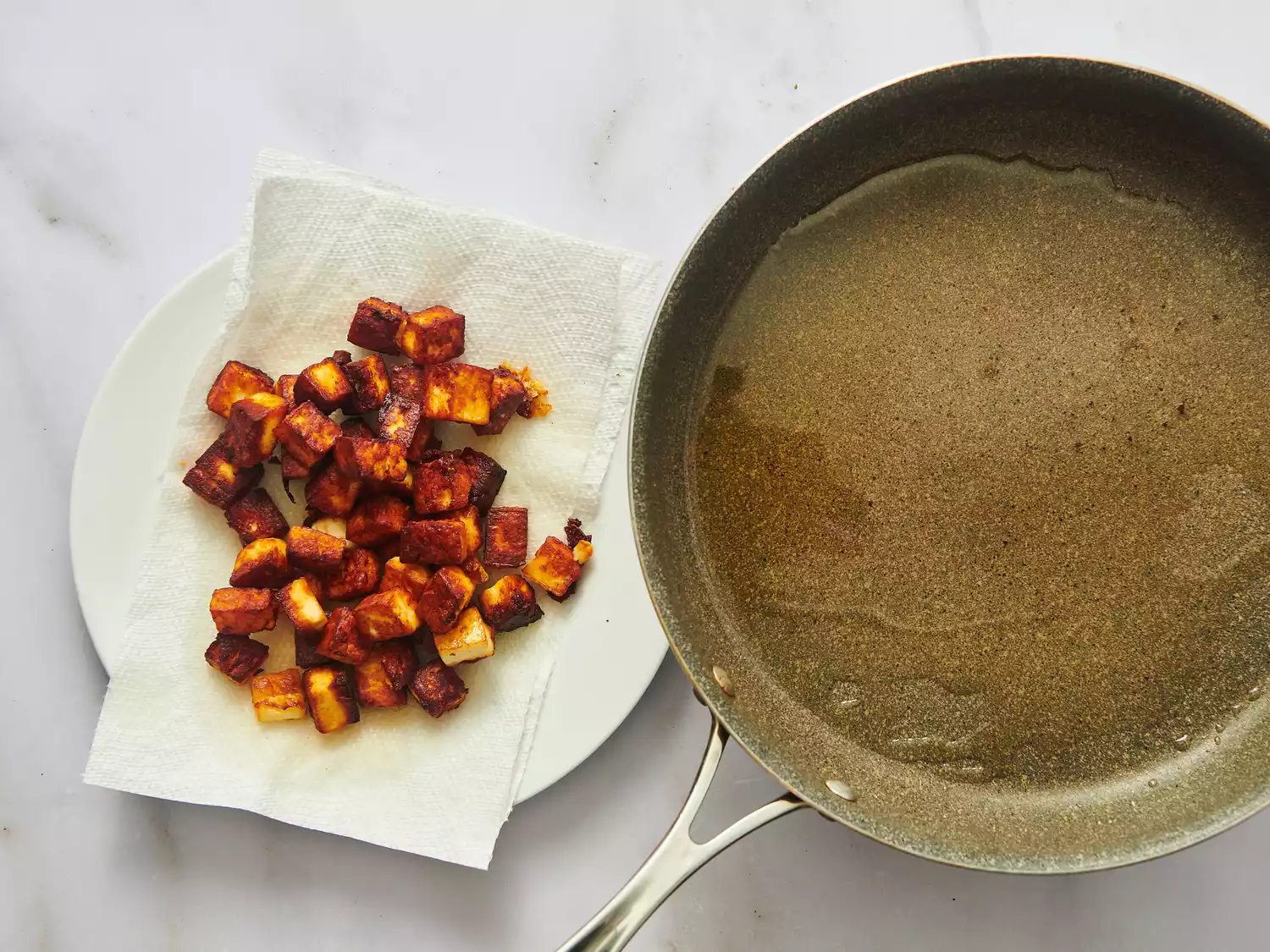 Cooked paneer cubes set aside on a plate next to a frying pan