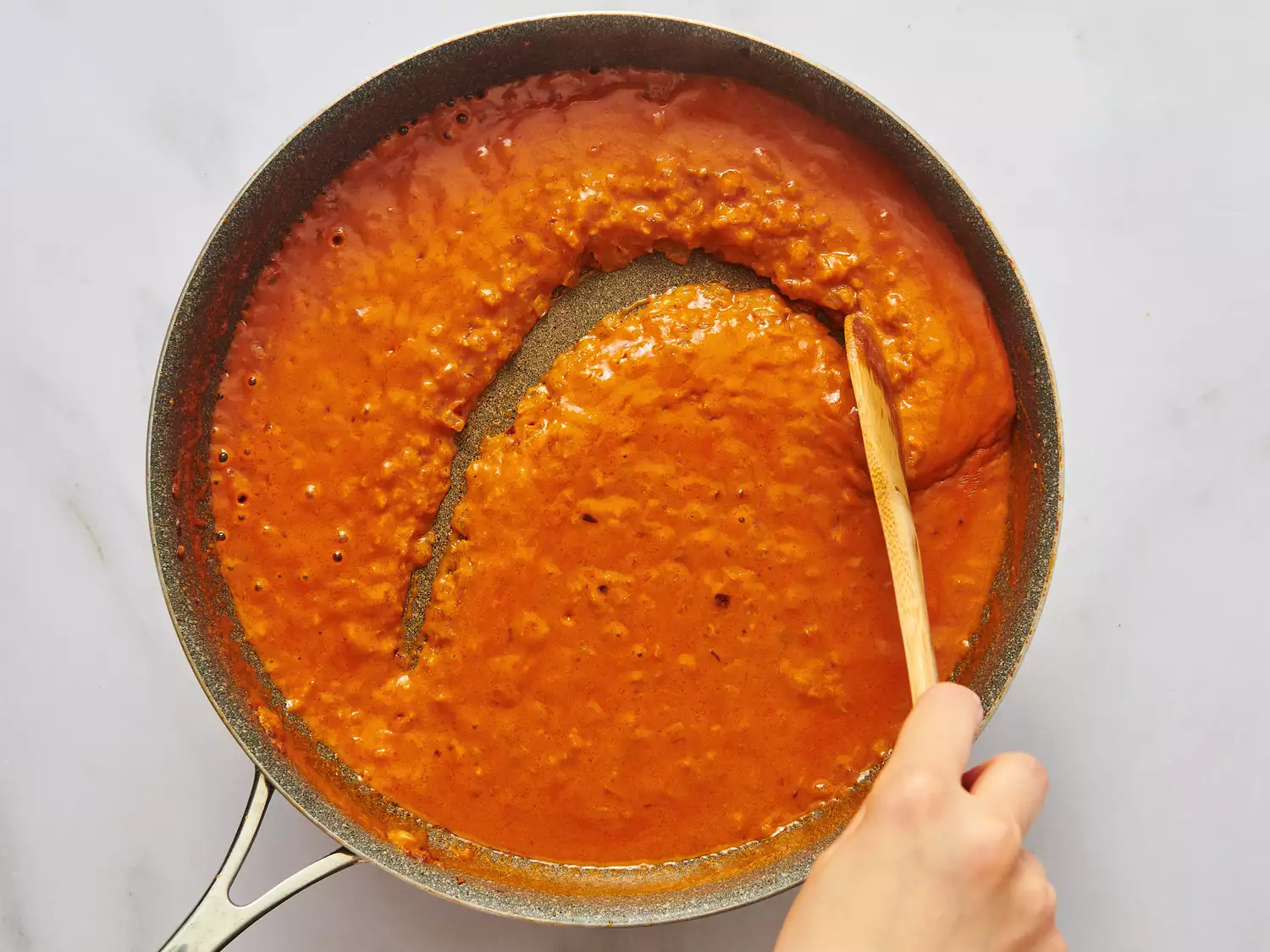 A person stirring a sauce in a frying pan with a wooden spoon