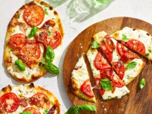 An overhead view of three naan bread margherita pizza with prosciutto, one sliced into four pieces.