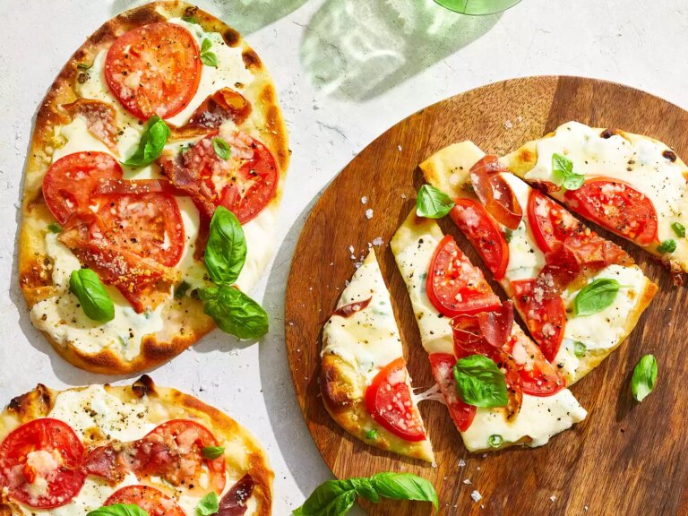 An overhead view of three naan bread margherita pizza with prosciutto, one sliced into four pieces.