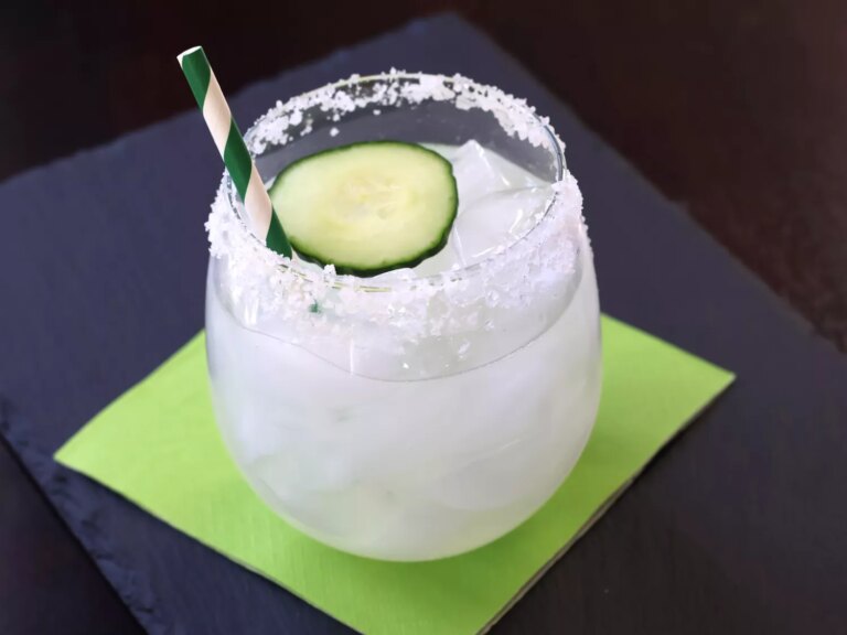Margarita on the rocks with salt rim, cucumber slice for garnish and green and white striped straw