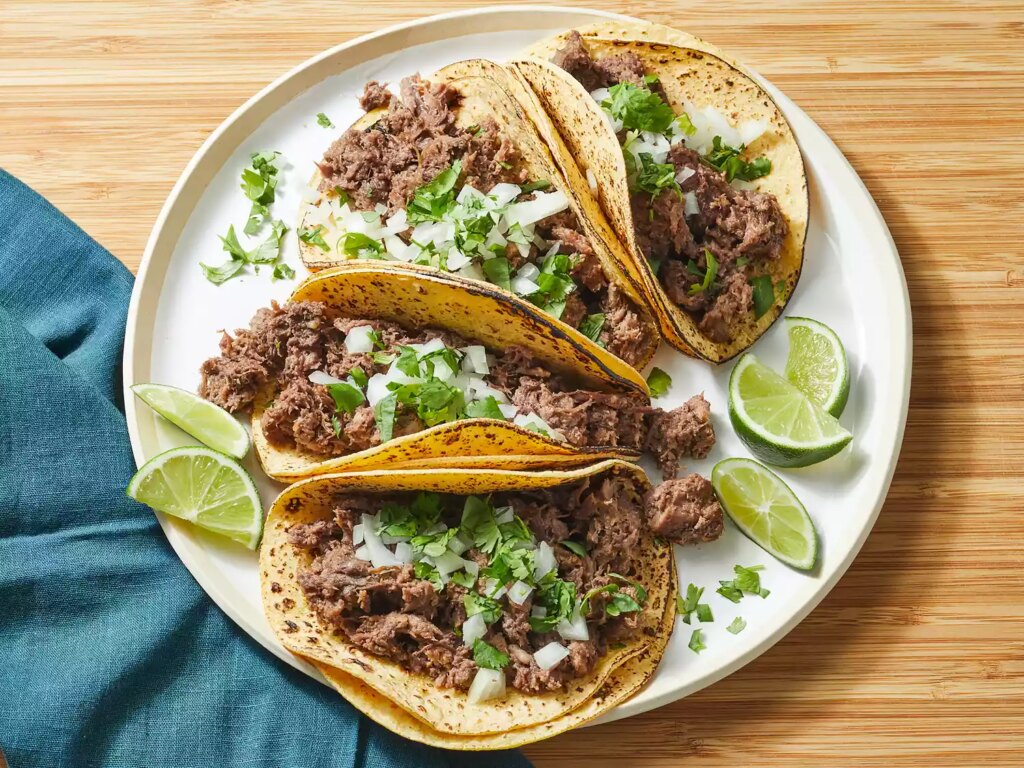 Looking down at a plate of slow cooker lengua tacos, topped with cilantro and white onion.