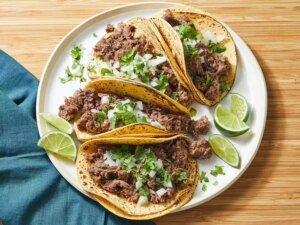 Looking down at a plate of slow cooker lengua tacos, topped with cilantro and white onion.