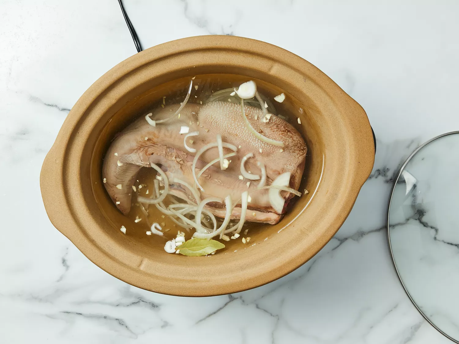 Beef tongue, onion, garlic, bay leaf, salt and water placed in a slow cooker.