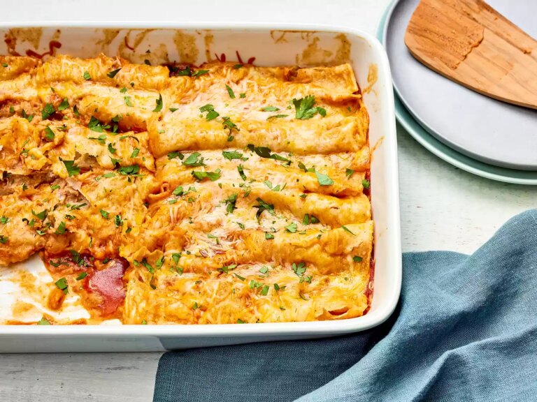 Refried bean and cheese enchiladas garnished with fresh herbs in a white baking dish
