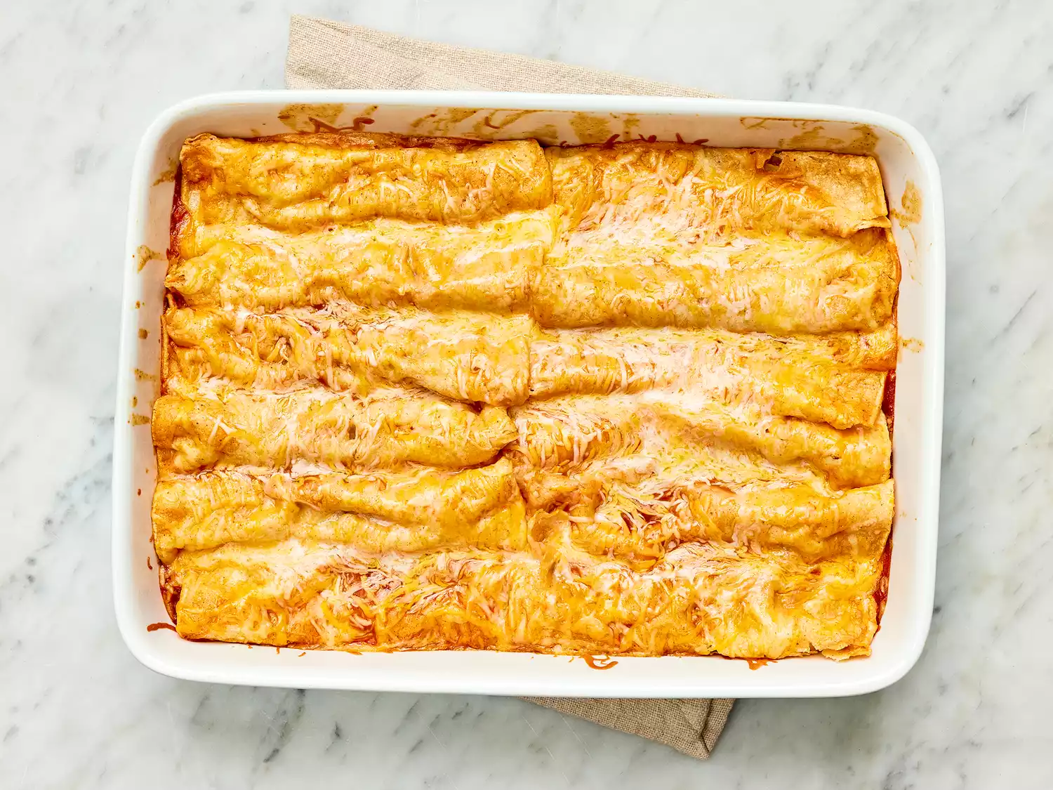 Baked Refried Bean and Cheese Enchiladas in a white casserole dish 