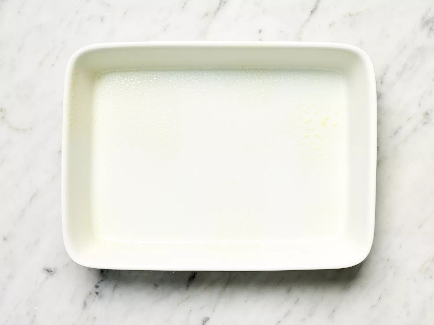 Greased white casserole dish on a marble counter 
