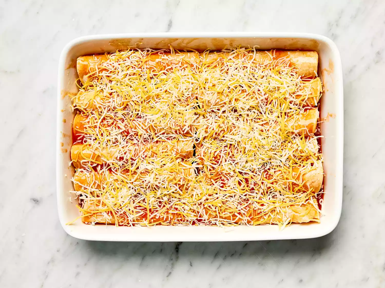 Refried Bean and Cheese Enchiladas covered with cheese in a white casserole dish 