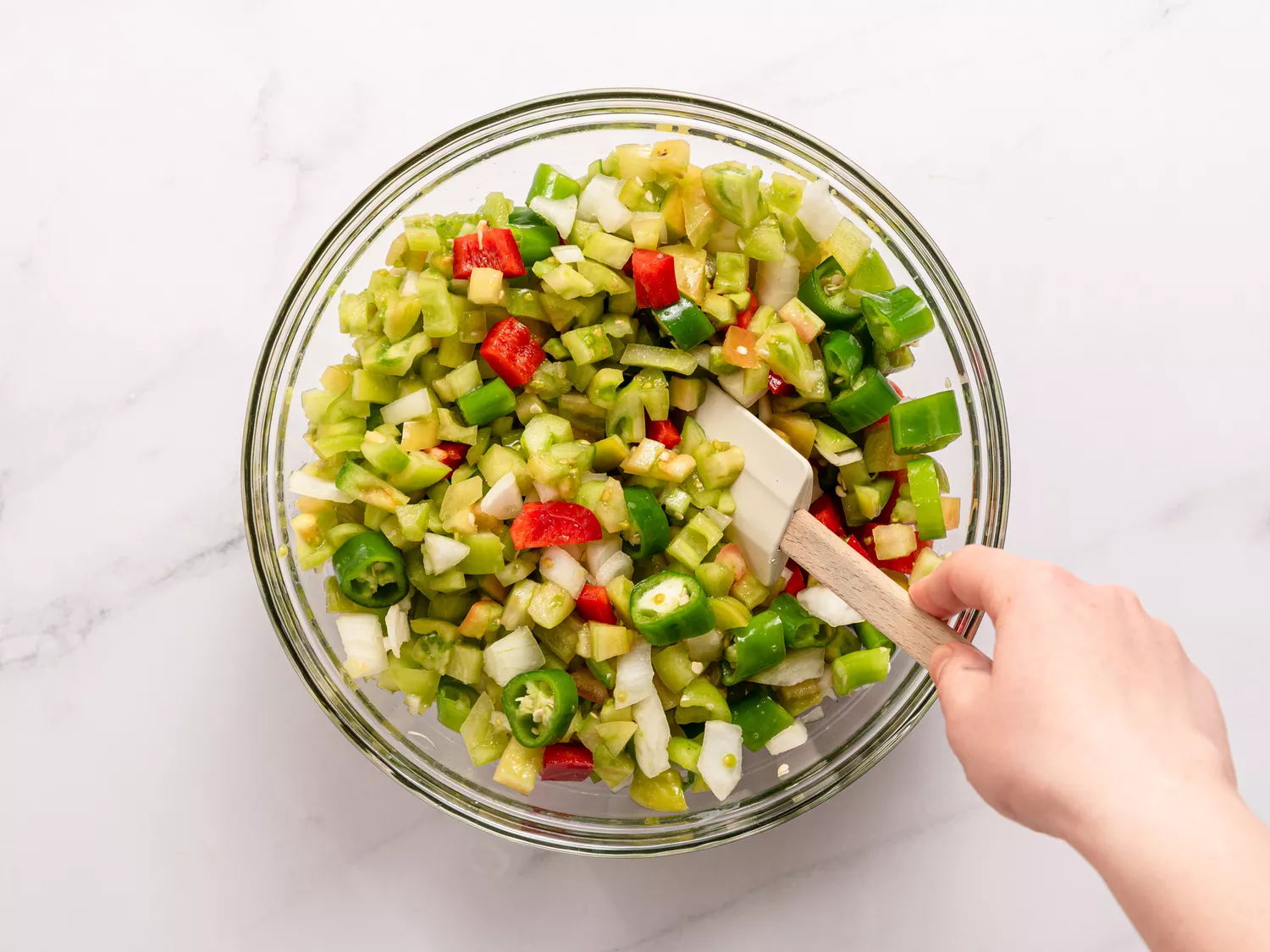 A glass bowl of diced vegetables being mixed with a spatula