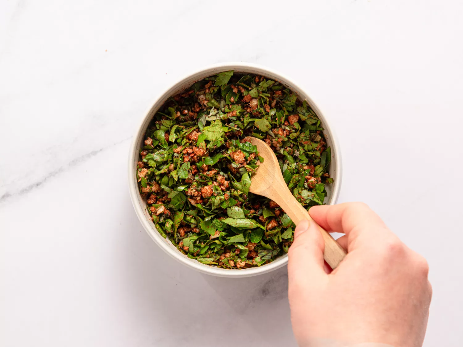 Hand mixing green salsa with a wooden spoon in a bowl
