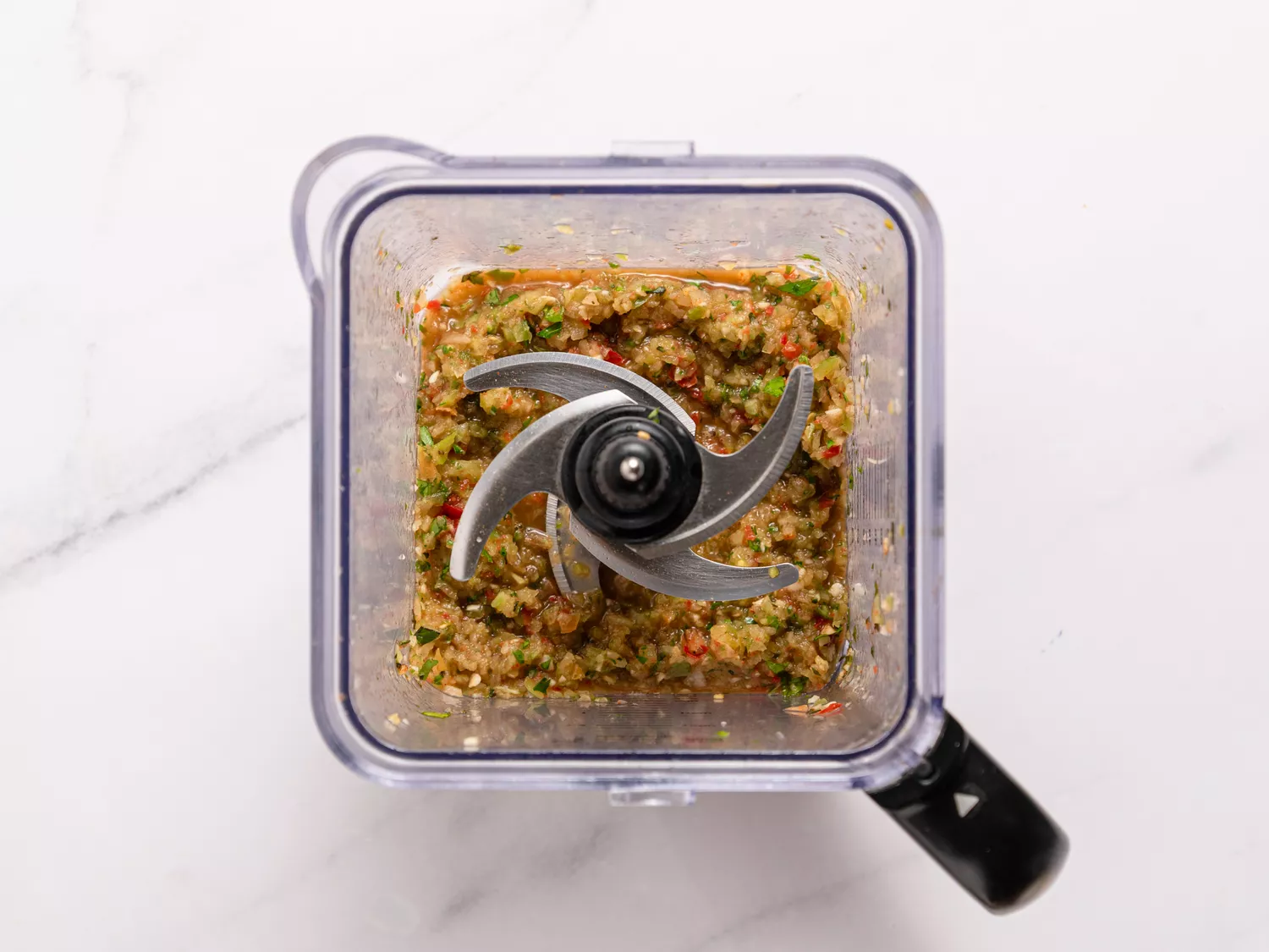 Blender container with blended green tomato salsa
