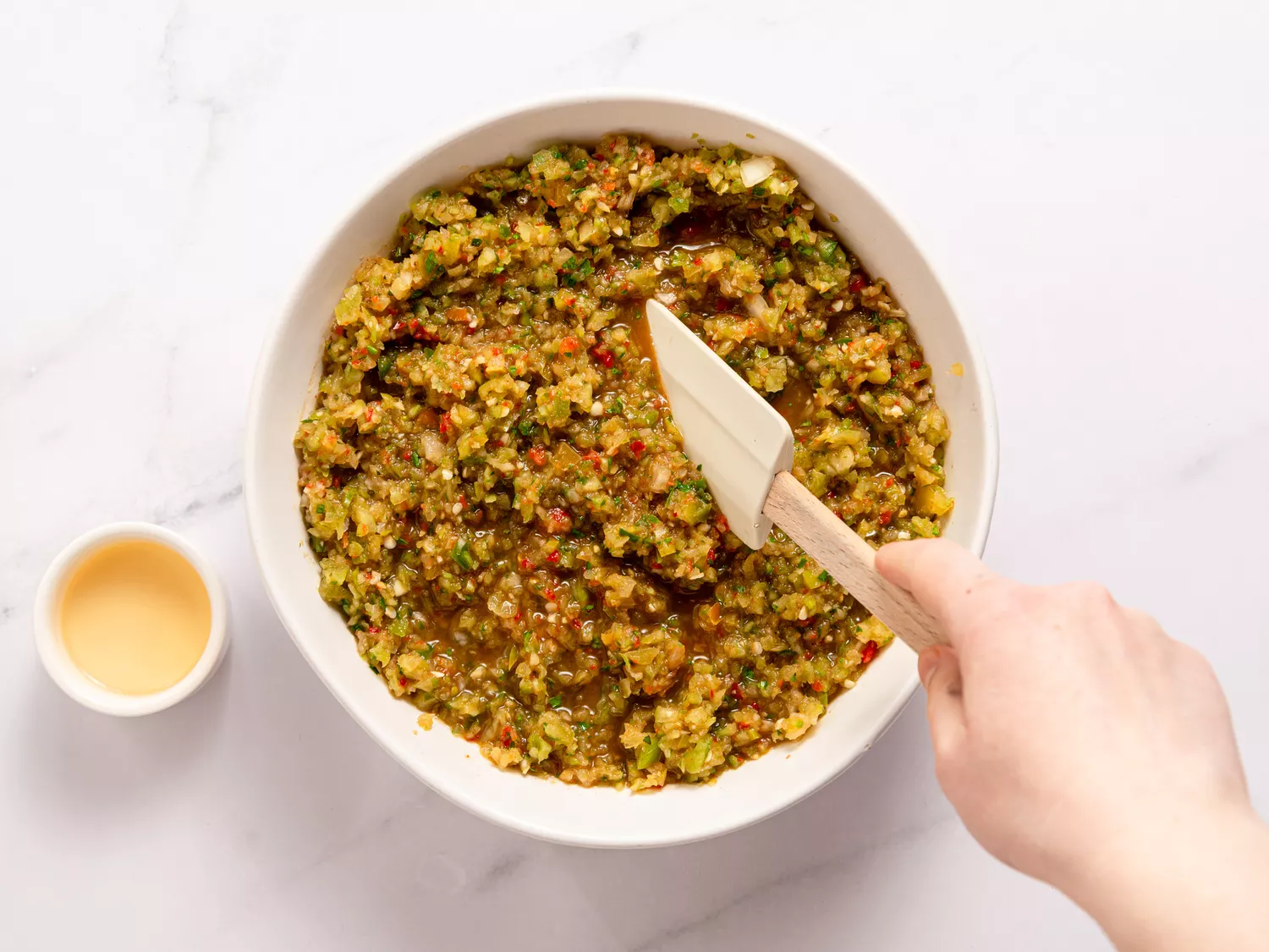 A hand mixing a green tomato salsa in a bowl with a spatula