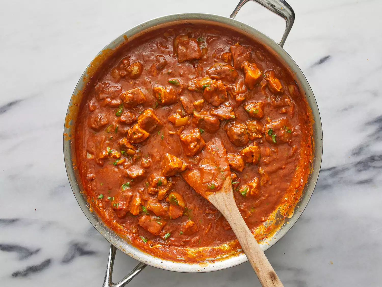 an overhead shot of chicken tikka masala in a skillet with a wooden spoon