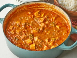 A pot containing paneer tikka masala prepared in rich sauce and served with rice in the background