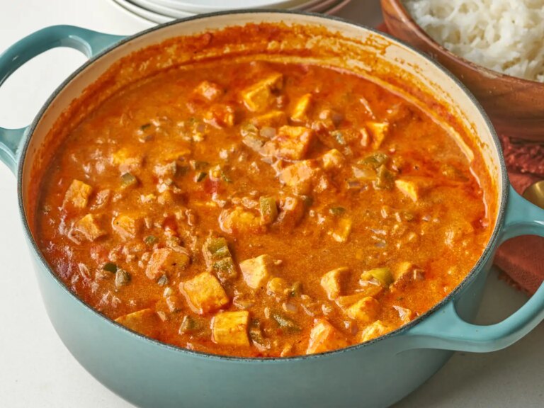 A pot containing paneer tikka masala prepared in rich sauce and served with rice in the background