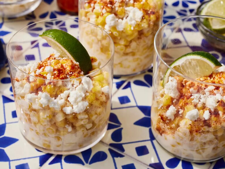 High angle looking at a few corn in a cups garnished with lime wedges, hot sauce and cheese