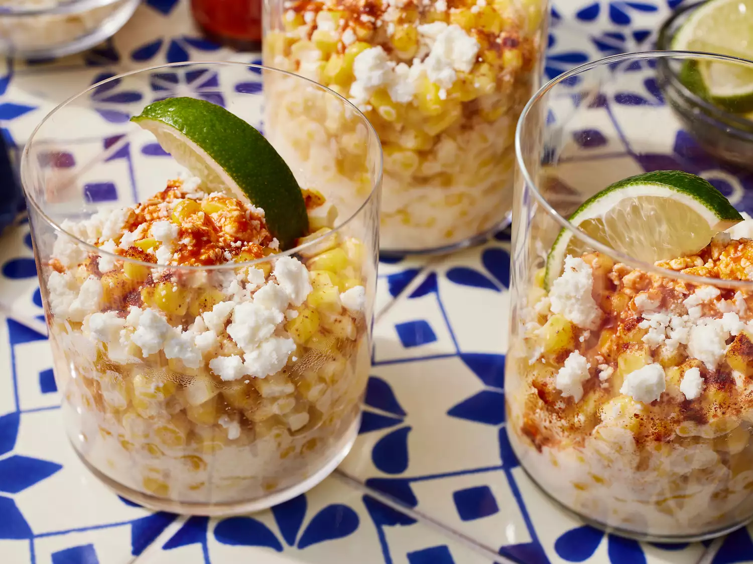 High angle looking at a few corn in a cups garnished with lime wedges, hot sauce and cheese