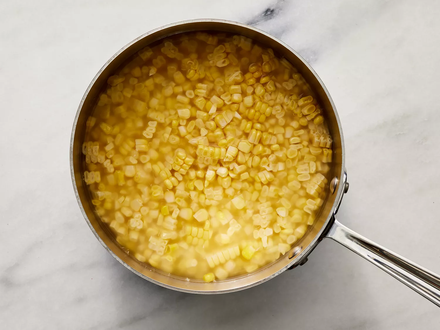 a top down view of corn kernels in a sauce pan, covered with water. 