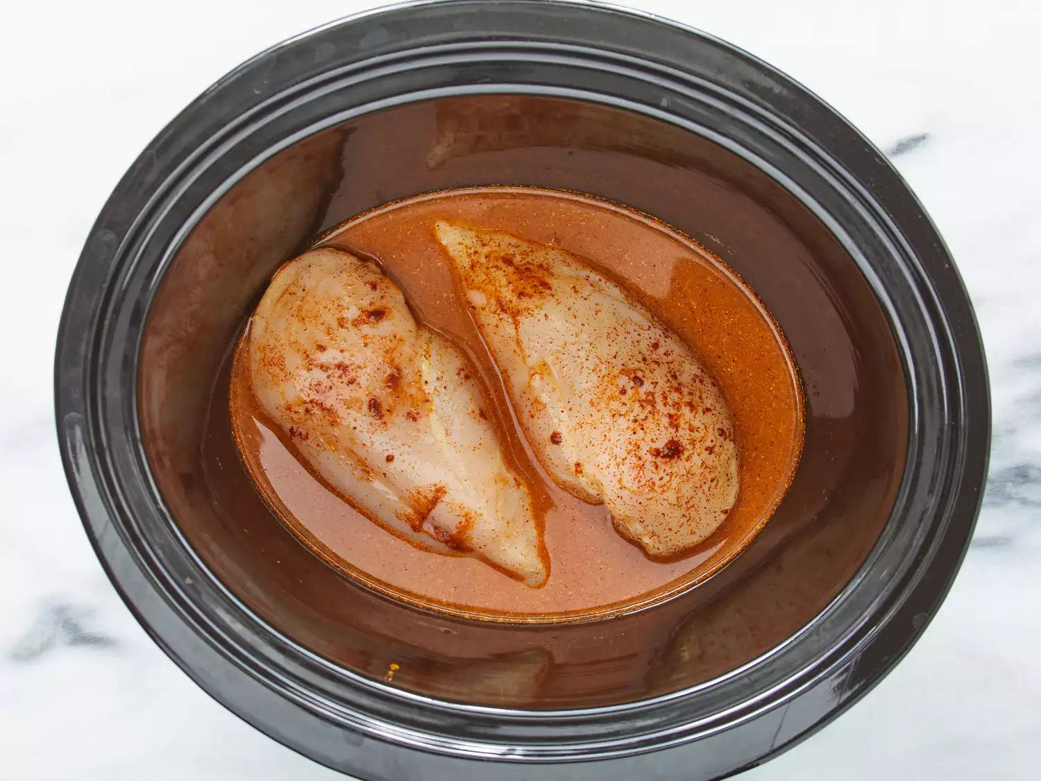 an overhead shot of two chicken breasts with sauce in a crock pot