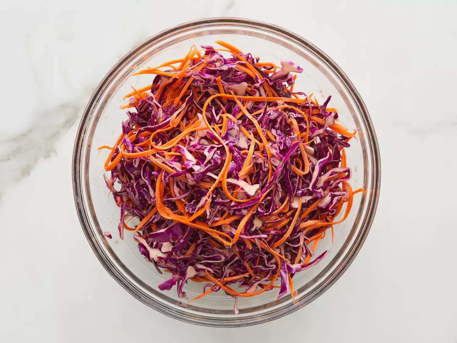 Overhead shot of a mixing bowl with shredded red cabbage, carrots, and other ingredients for tacos