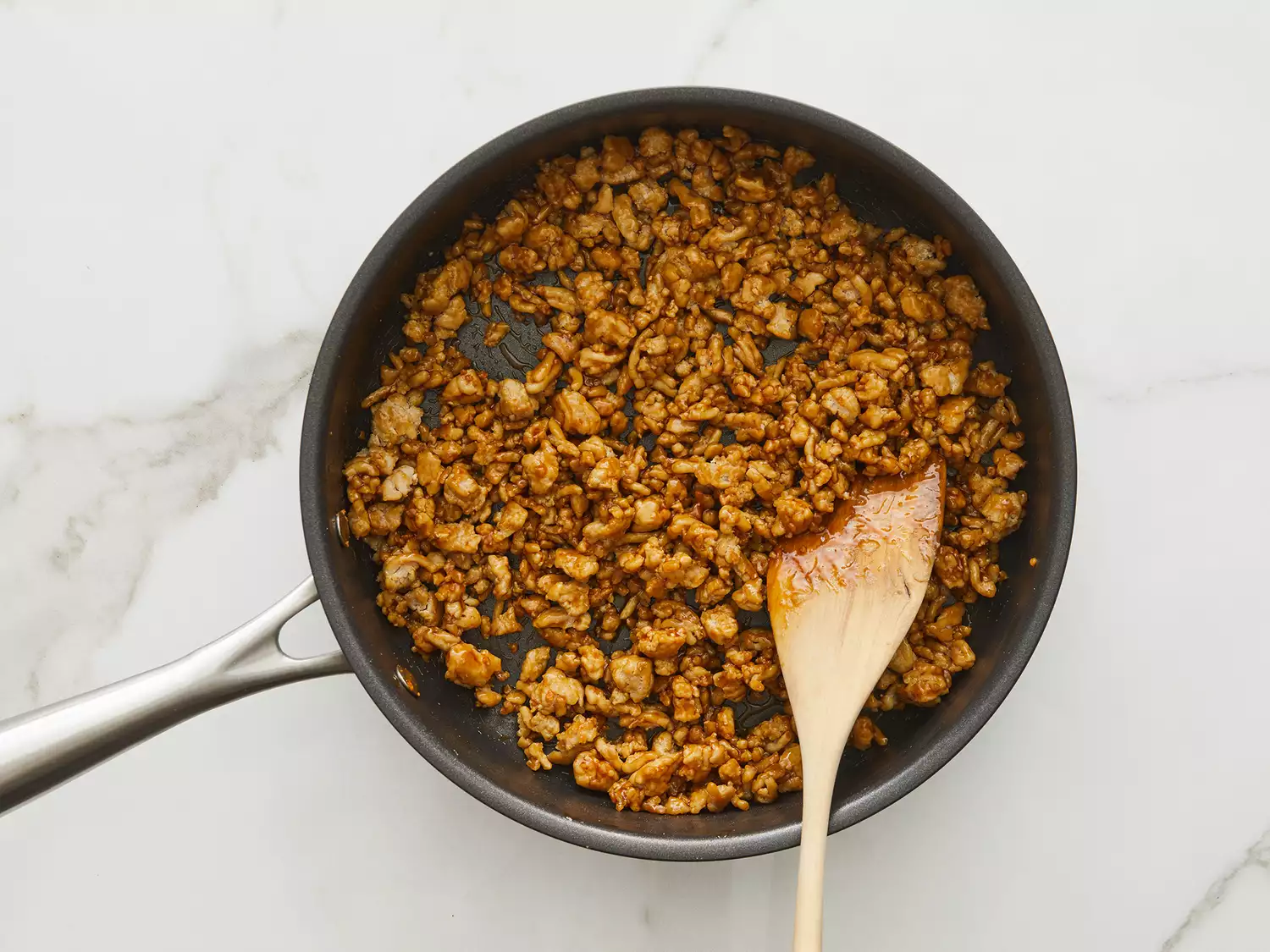 Overhead shot of a pan with ground chicken cooking and being stirred with a wooden spoon