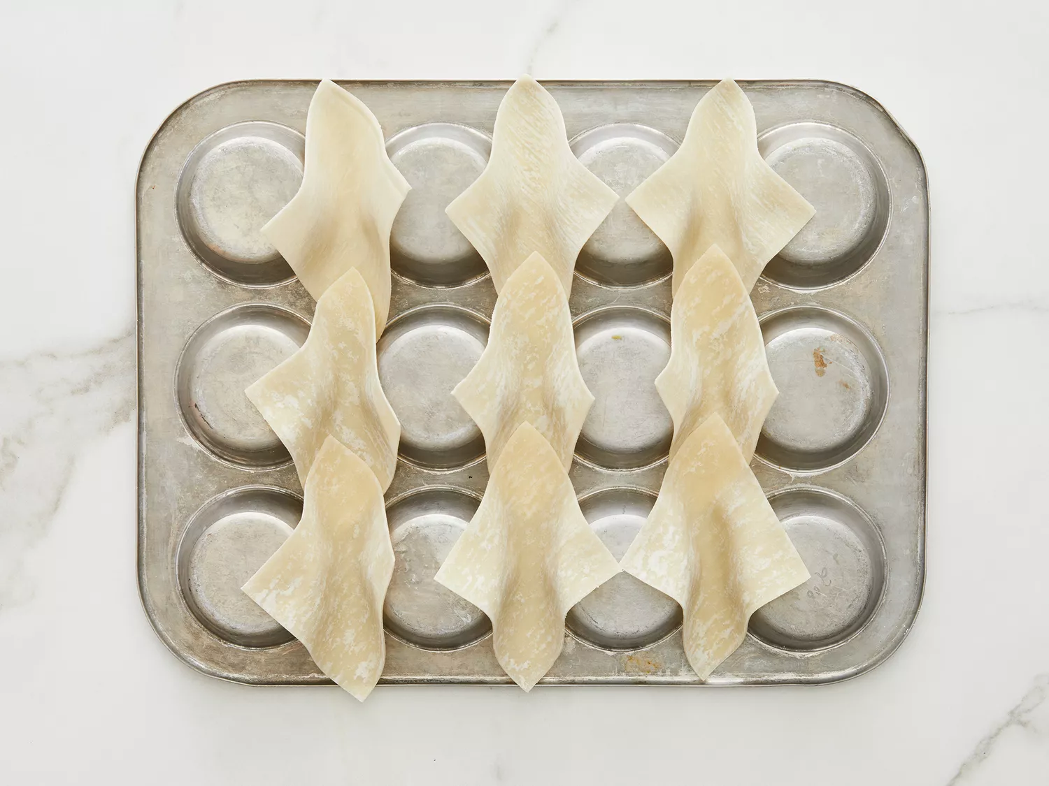 High angle shot of an upside-down muffin tin holding wonton wrappers that have been folded like taco shells