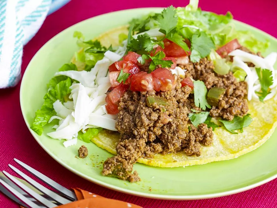 Close up view of a taco de matamoros with tomatoes and lettuce on a green plate