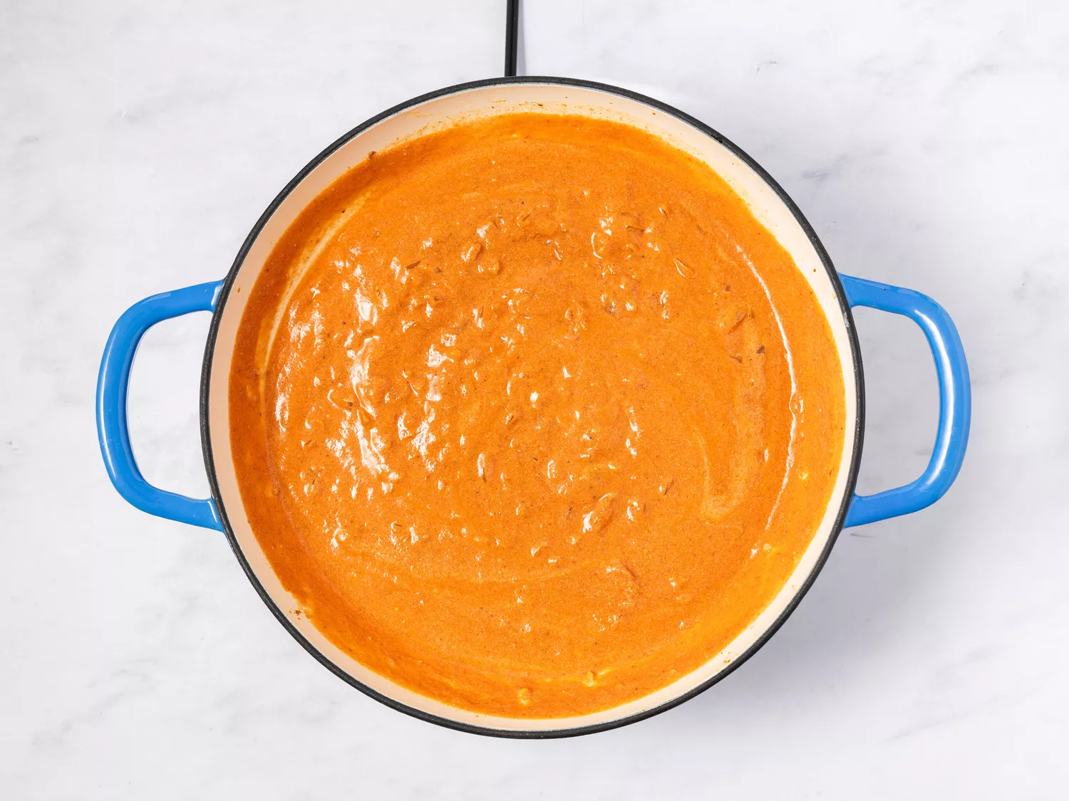 A pot of Indian butter chicken in progress, cooking in a light-colored sauce until creamy and smooth