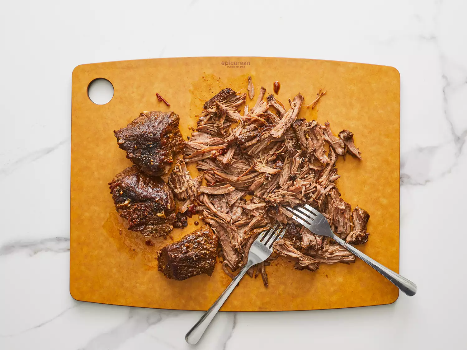Overhead of beef on a cutting board being pulled apart with two forks. 