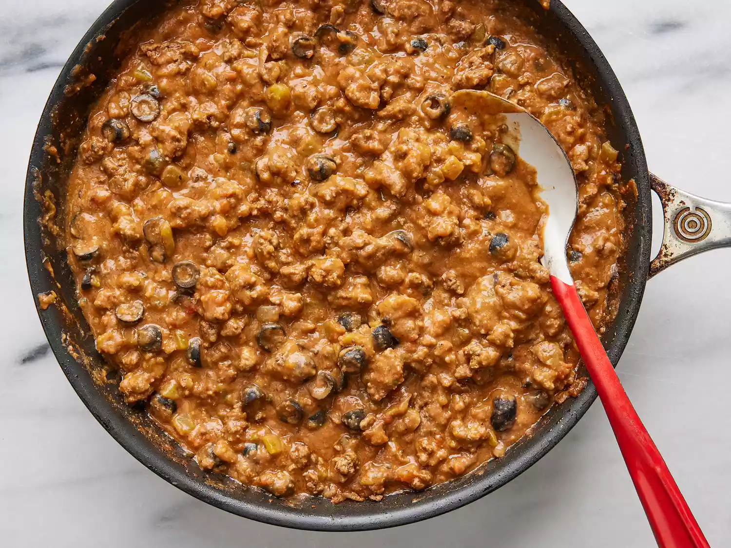 Overhead of taco casserole meat cooking in a skillet being stirred by a spoon. 