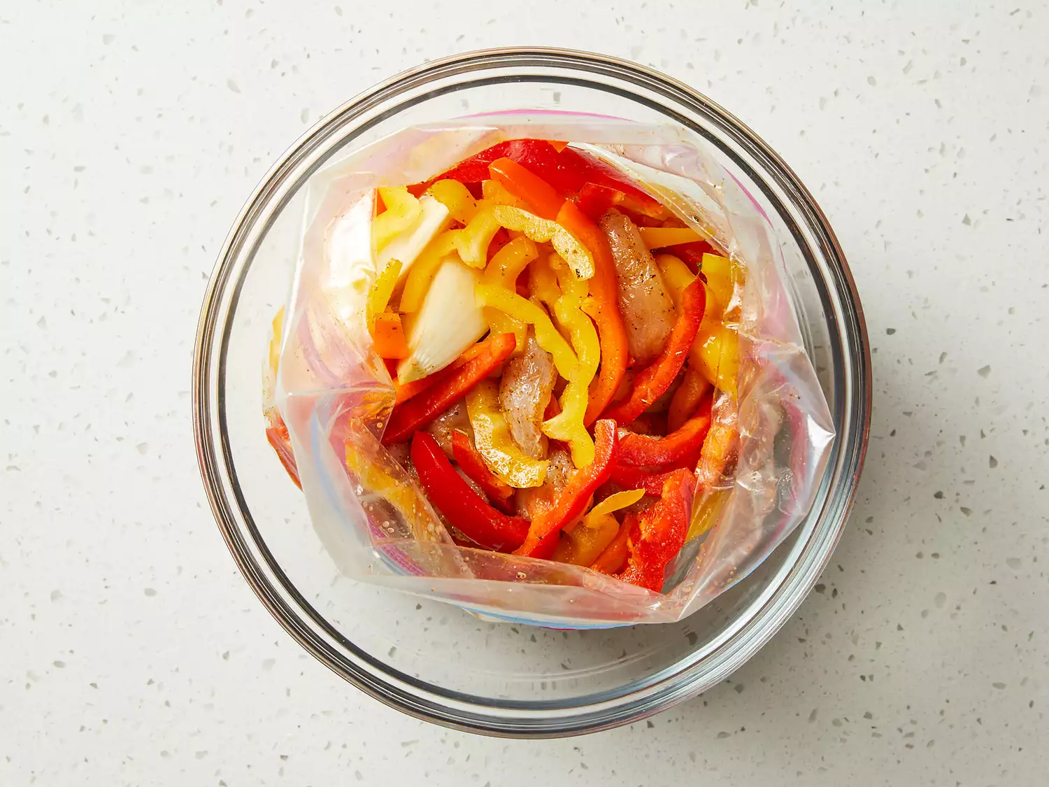 an overhead shot of bell peppers, chicken, and marinade combined in a plastic bag