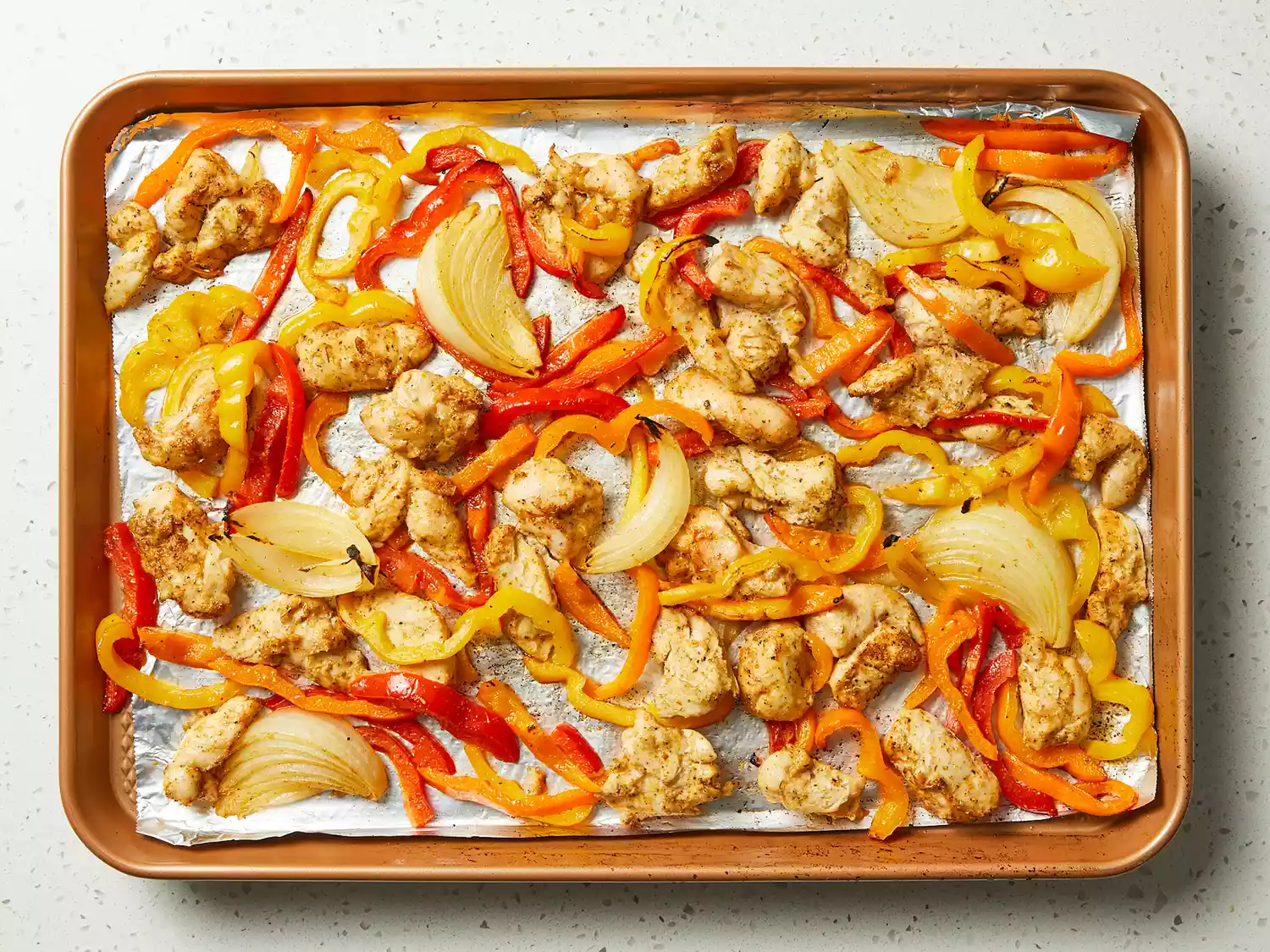 an overhead shot of cooked chicken fajitas on a sheet pan
