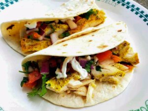 Close up view of mahi mahi fish tacos with tomatoes and fresh herbs on a white plate