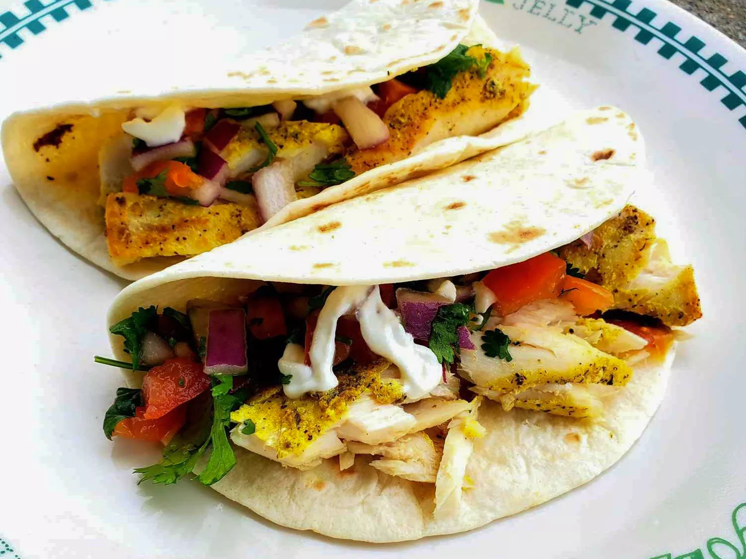 Close up view of mahi mahi fish tacos with tomatoes and fresh herbs on a white plate