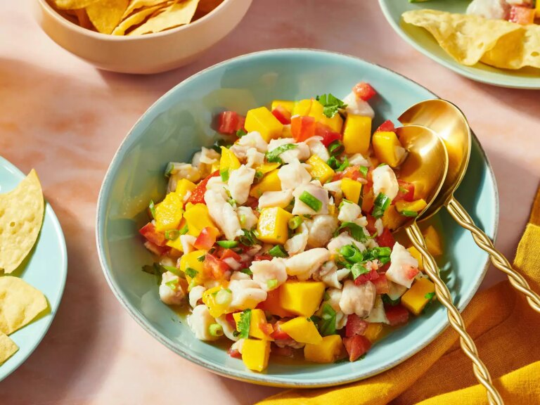 Mexican mango and white fish ceviche in a bowl with a spoon, surrounded by tortilla chips