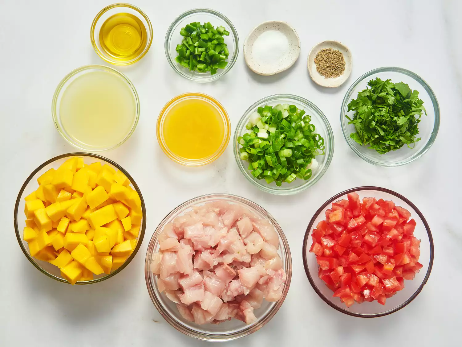 Ingredients for mango and white fish ceviche prepared in small bowls, including fish, mango, tomato, herbs, and seasonings