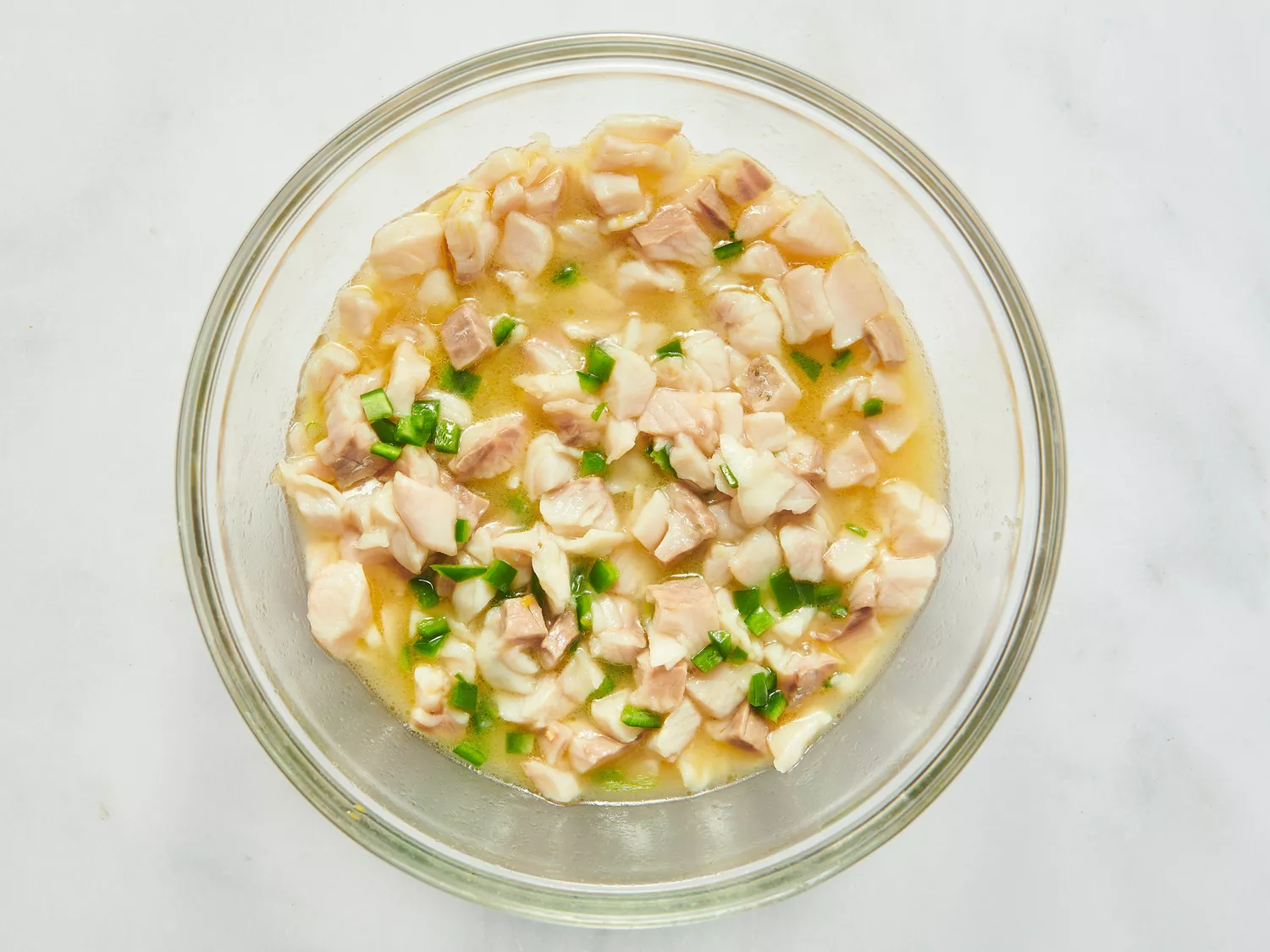 Glass bowl containing diced fish and green garnish immersed in citrus juices