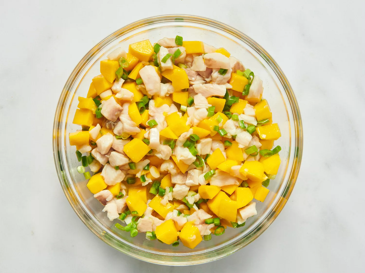 A glass bowl containing mango and white fish ceviche mixed with herbs