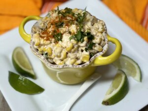 Elotes mexocan corn in a yellow cup garnished with lime wedges
