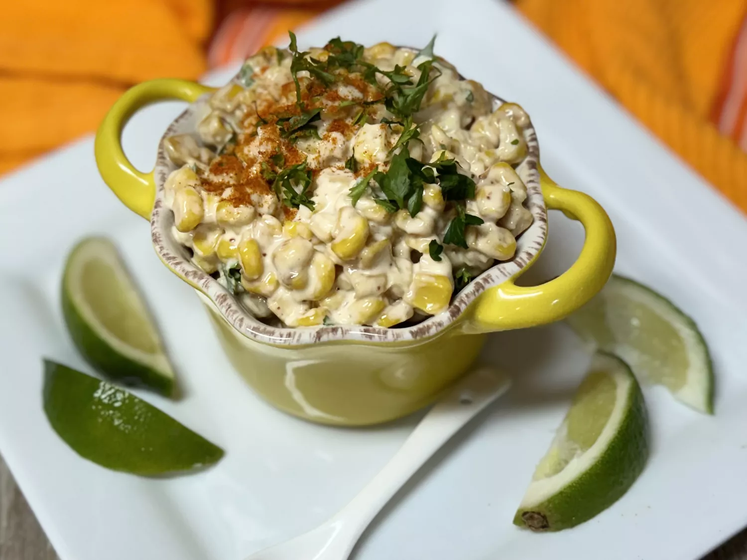 Elotes mexocan corn in a yellow cup garnished with lime wedges